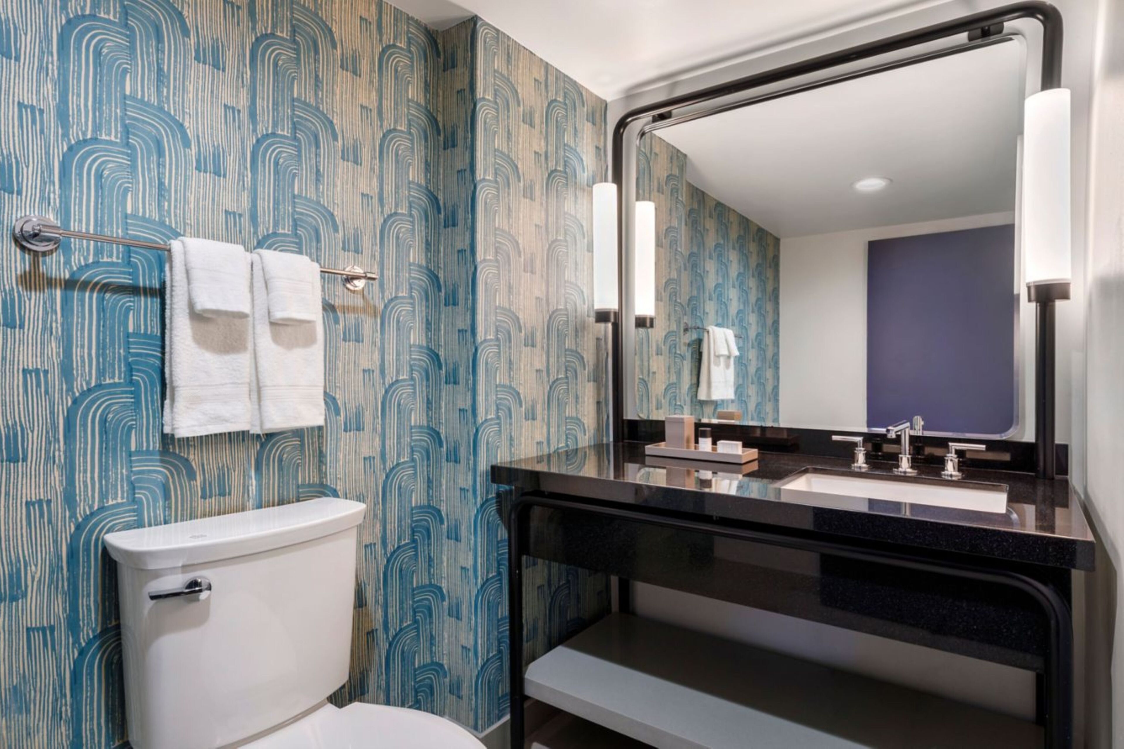 A bathroom with a toilet, a sink with a mirror, and patterned wallpaper.