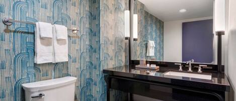 A bathroom with a toilet, a sink with a mirror, and patterned wallpaper.
