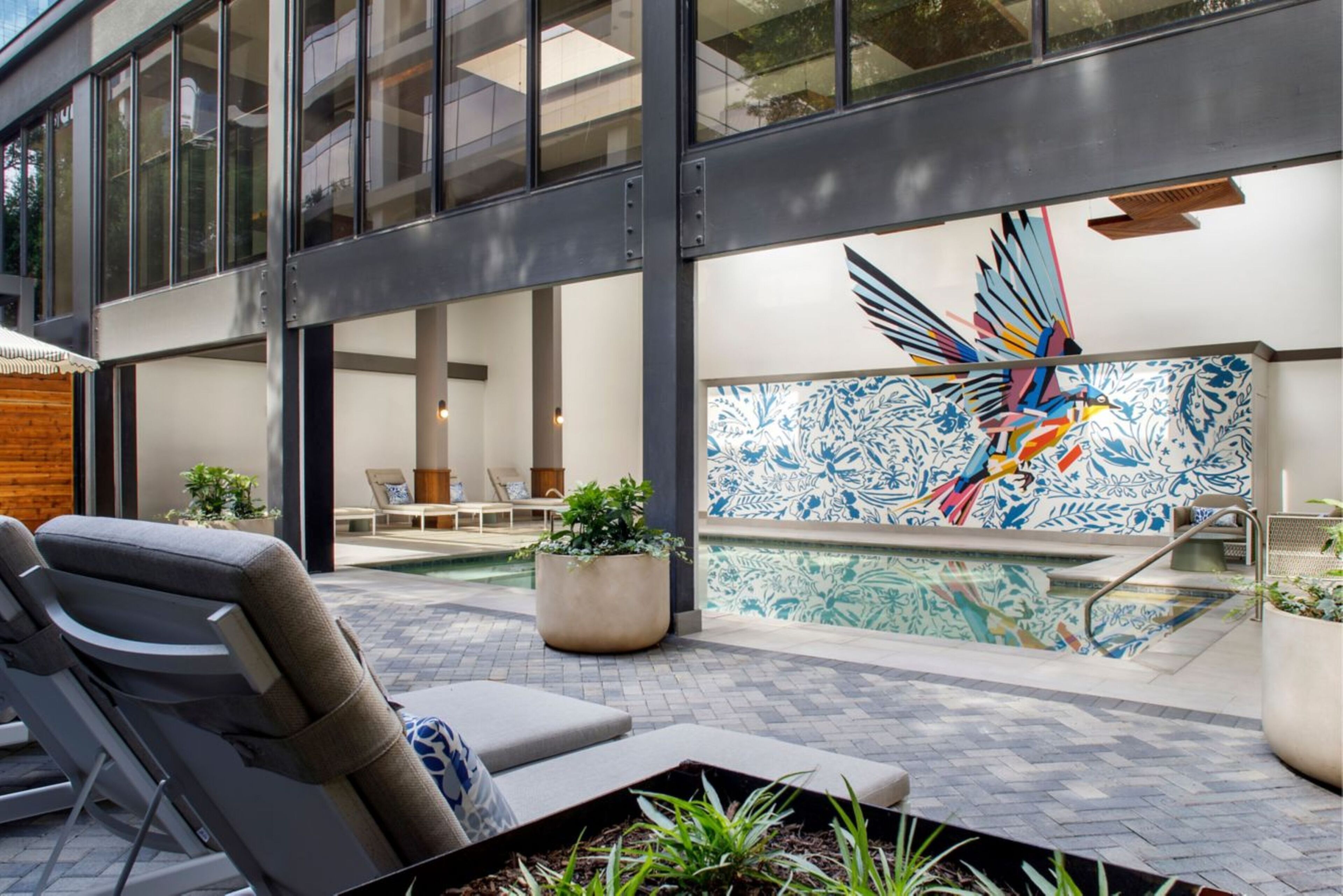 A modern outdoor pool area with lounge chairs, a decorative wall mural, and a clear view of the pool.