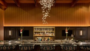 Una zona de bar con una barra larga, varios taburetes y una estantería bien surtida con diferentes botellas.