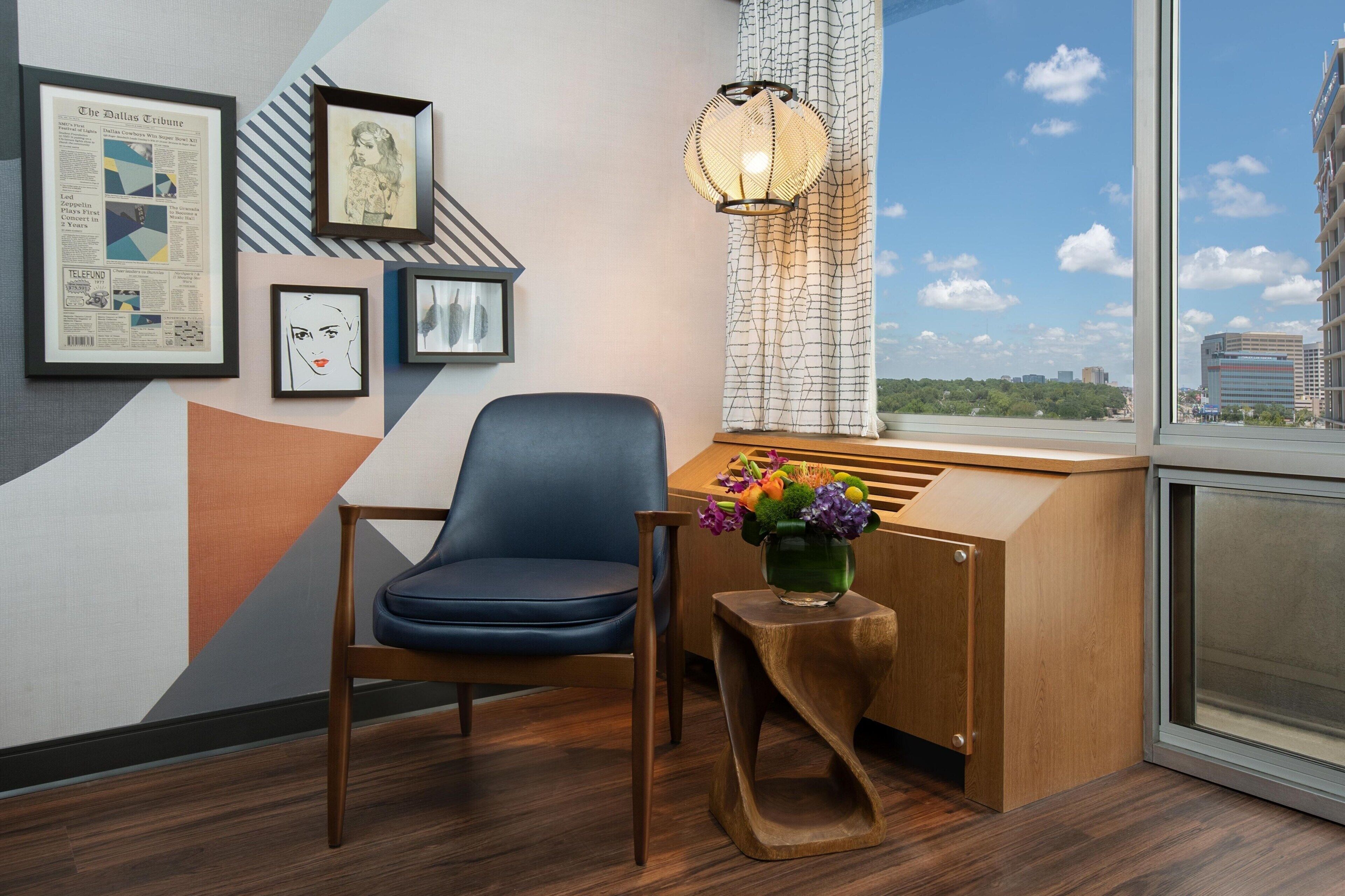 A modern room with a blue chair, a wooden desk, a vase with flowers, and framed pictures on the wall.