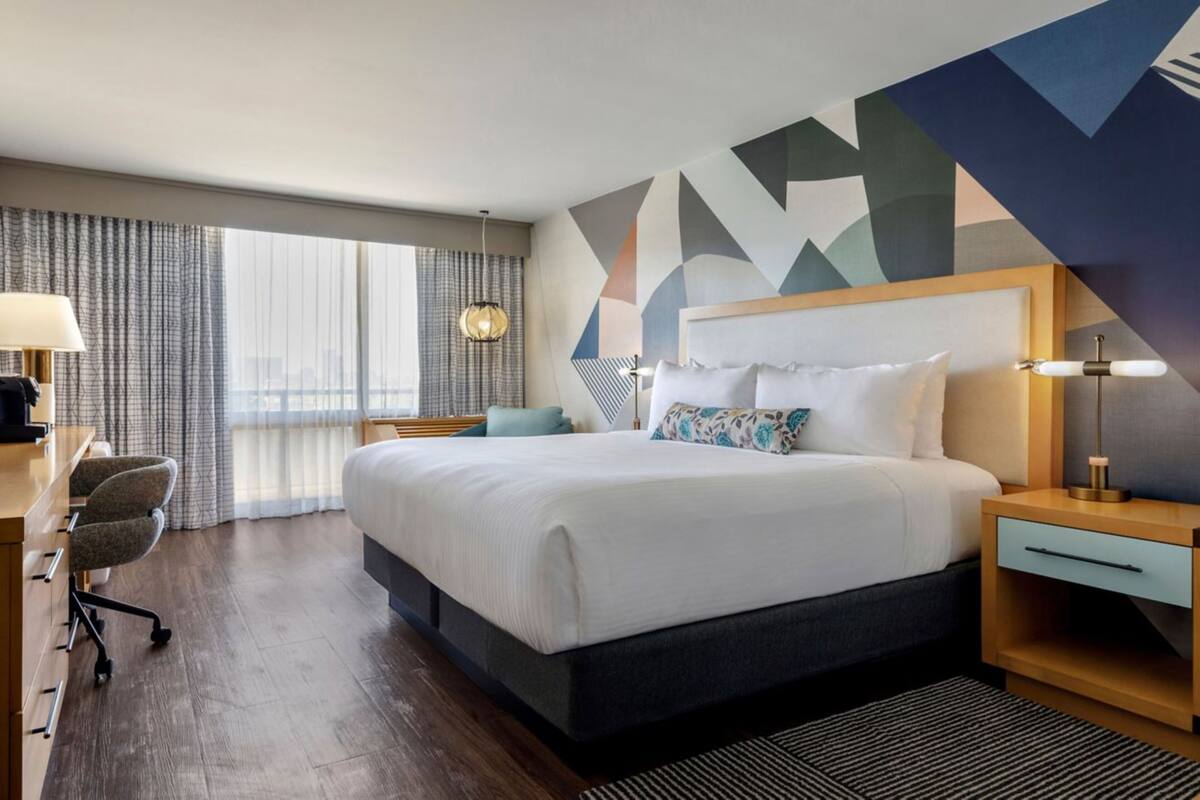 A hotel room with a large bed, a desk, a chair, and a view of the city through the window.