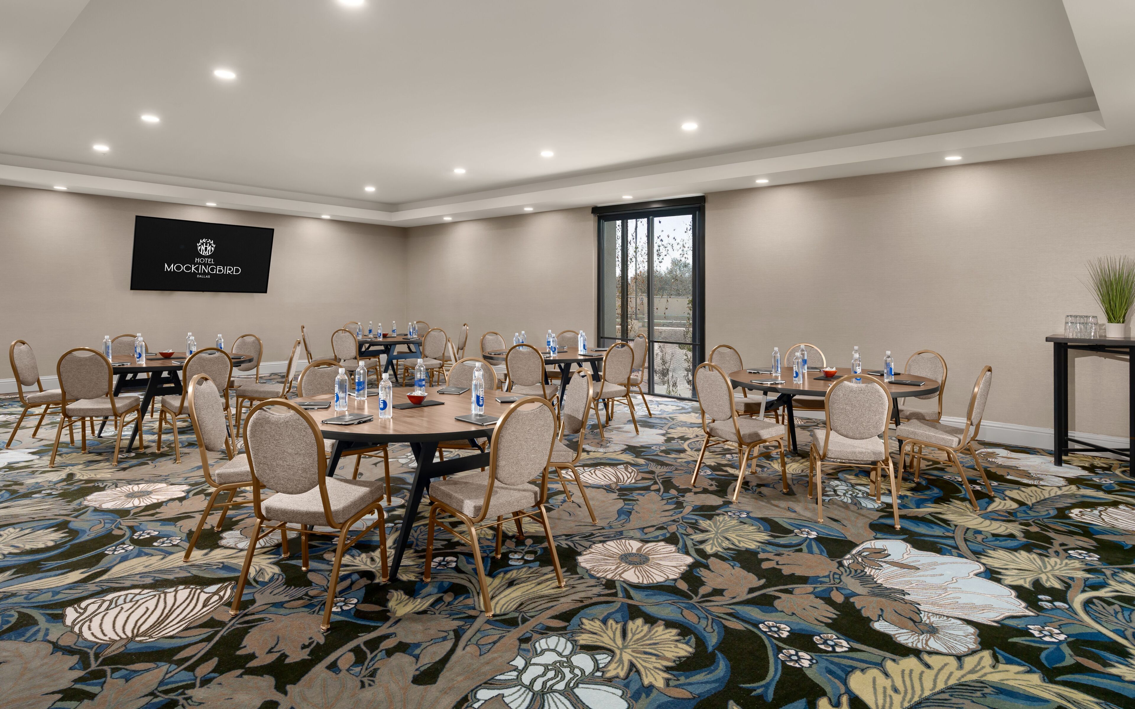 Une salle de conférence équipée de tables rondes, de chaises et d’un grand écran affichant le nom de l’hôtel.