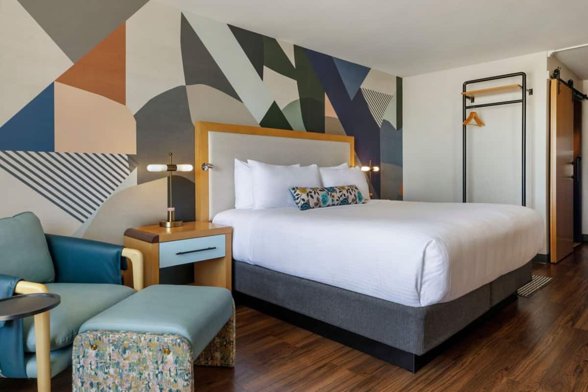 A hotel room with a bed, a desk, a chair, a small table, and a wardrobe.