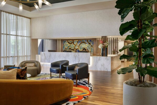 A hotel lobby with a reception desk, seating area, and a large plant.