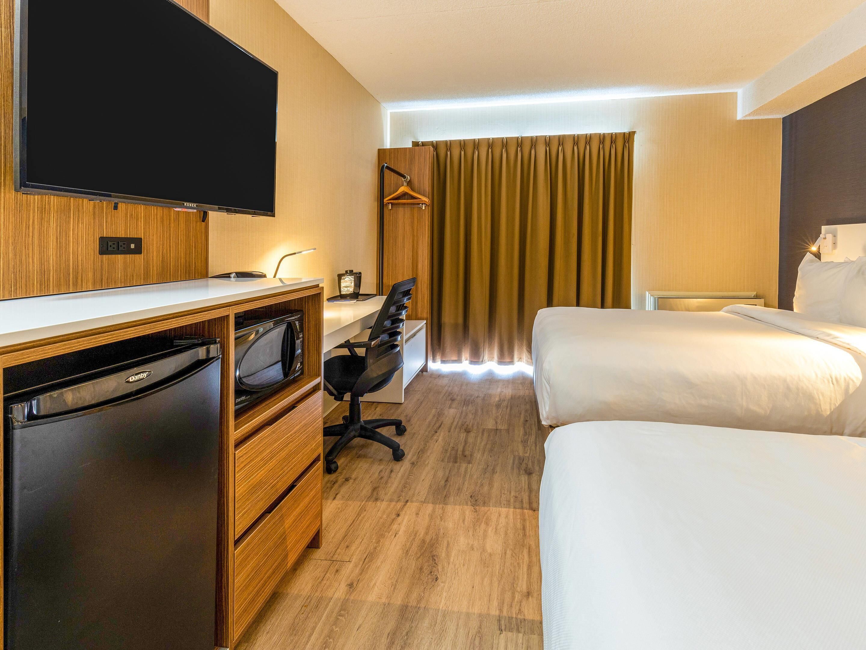 Habitación de hotel con televisión de pantalla plana, escritorio con computadora, silla, cama y armario.