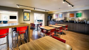 A modern restaurant with wooden tables and red chairs, a kitchen area, and framed artwork on the walls. - Comfort Inn Rouyn Noranda (Rouyn-Noranda)