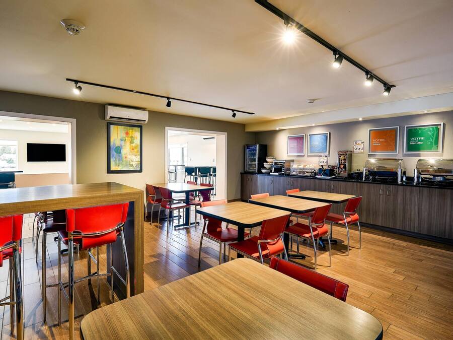 Un restaurante moderno con mesas de madera y sillas rojas, una zona de cocina y cuadros decorativos en las paredes.
