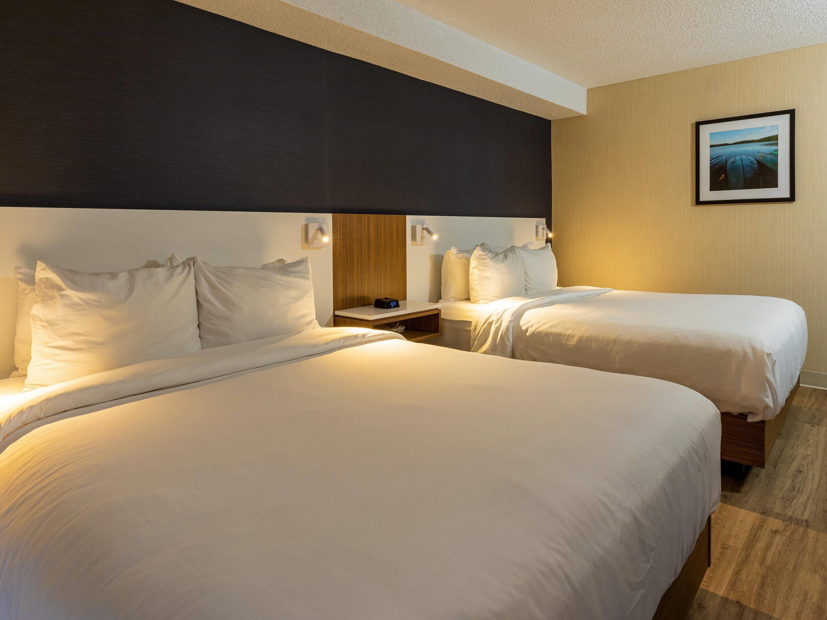 A hotel room with two beds, a nightstand, and a framed picture on the wall.