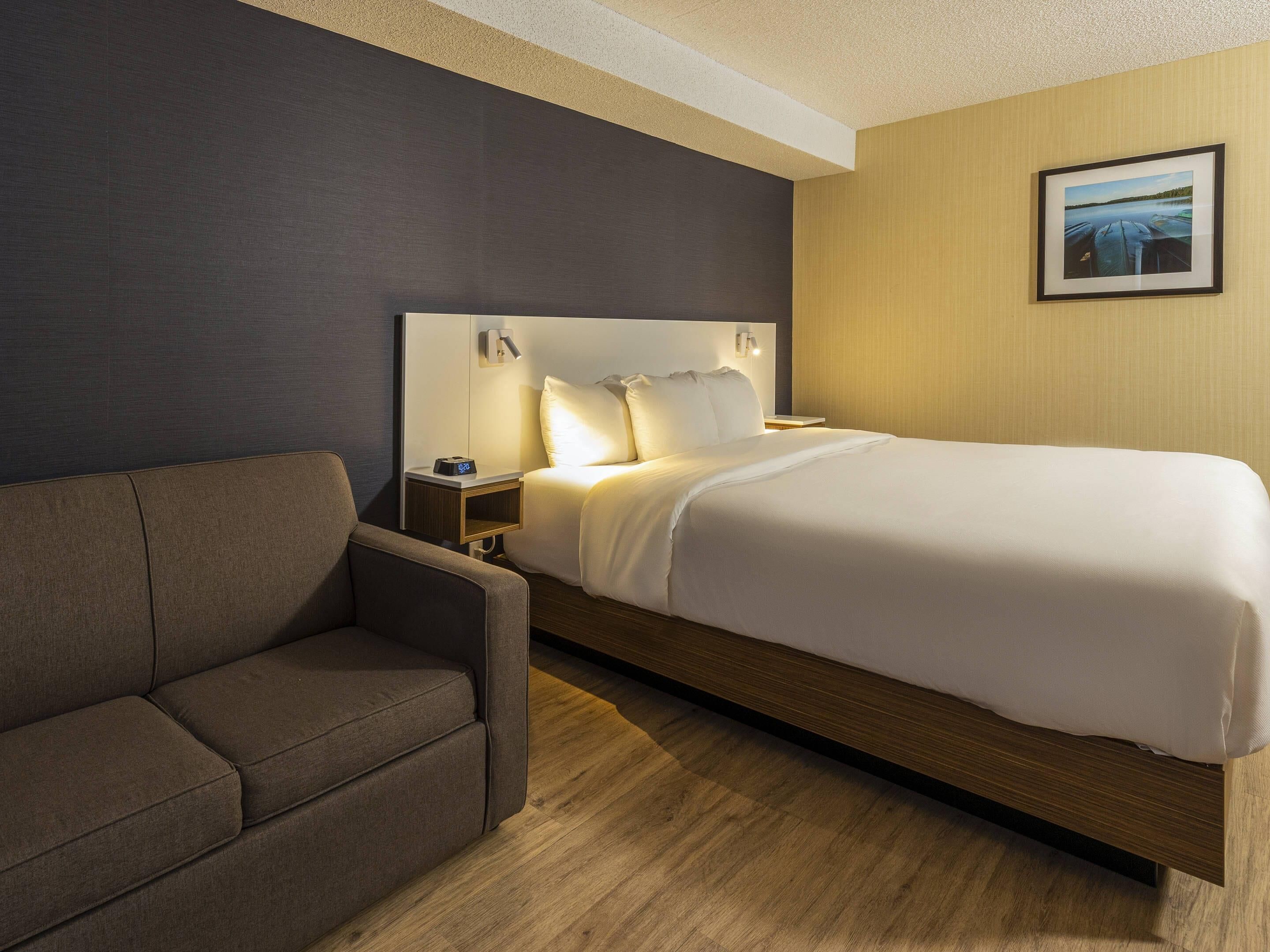 Ein Hotelzimmer mit einem großen Bett, einem Nachttisch mit Lampe, einer Couch und einem gerahmten Bild an der Wand.