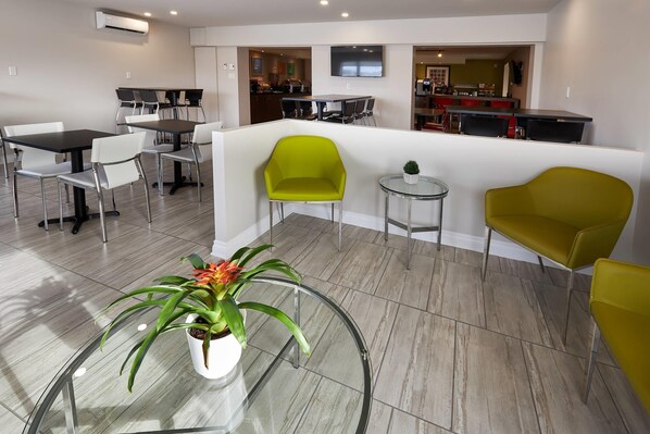 A modern dining area with a glass table, white chairs, and a green accent chair. A small round table with a potted plant is also visible.