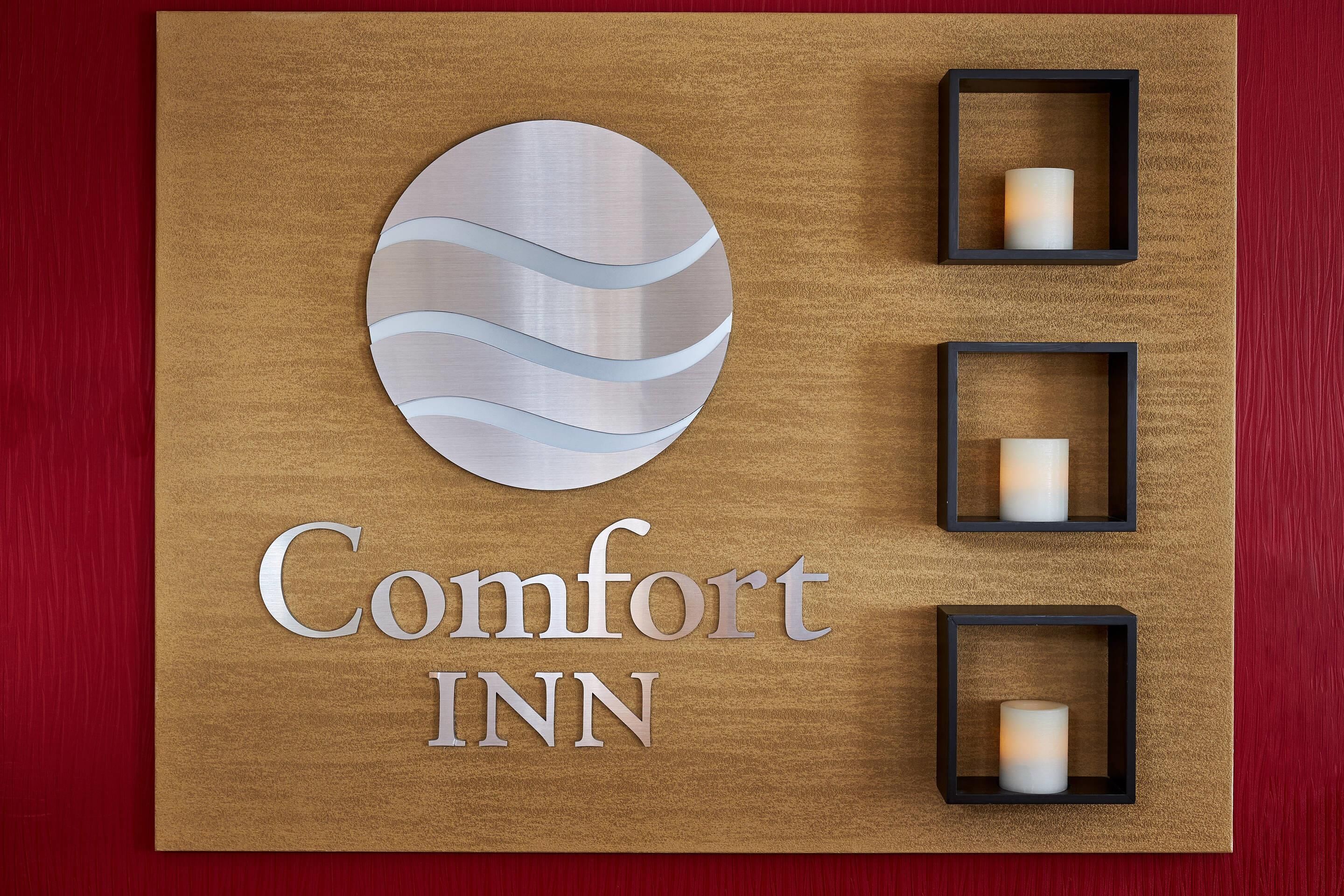 Ein hölzernes Schild mit der Aufschrift "Comfort INN" und drei kleinen, quadratischen Rahmen mit Kerzen.