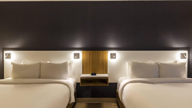A hotel room with two beds, a nightstand, and a wall-mounted light fixture. - Comfort Inn Rouyn Noranda (Rouyn-Noranda)