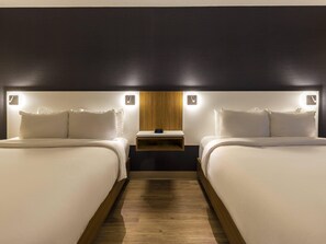 Una habitación de hotel con dos camas, una mesita de noche y una lámpara fijada a la pared.