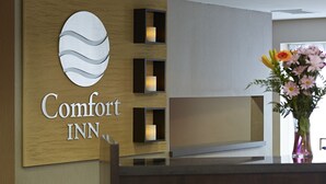 A reception area with a wooden panel wall displaying the Comfort Inn logo, a vase with flowers, and a modern design with recessed lighting. - Comfort Inn Rouyn Noranda (Rouyn-Noranda)