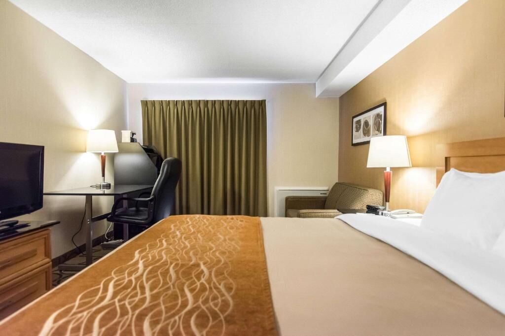 Habitación de hotel con cama, escritorio, silla, televisor, lámparas y una cortina.