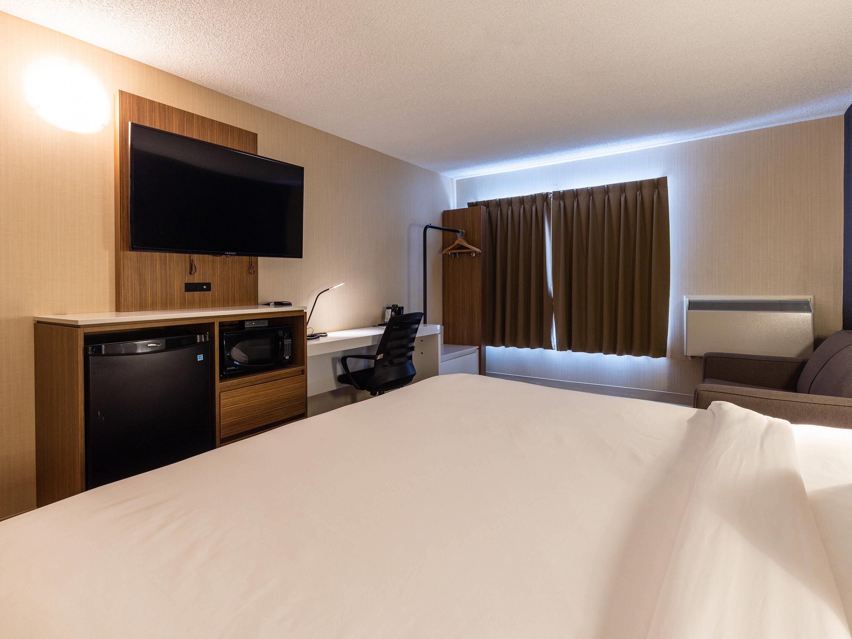A hotel room with a bed, a desk with a computer, a television, a microwave, and a mini-fridge.