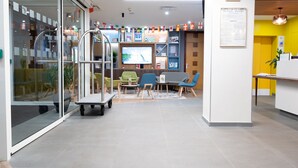 A reception area with a glass door, a cart, seating, and a TV screen.