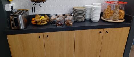 A kitchen counter with a toaster, a fruit basket, jars of nuts, and stacks of plates.