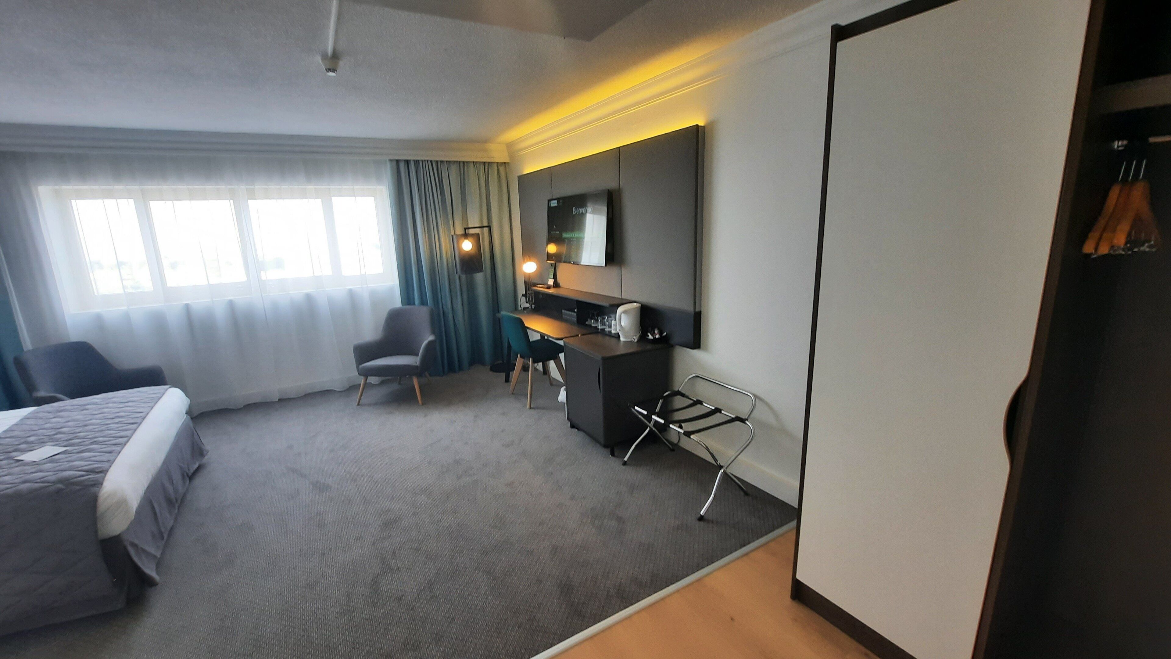Una habitación de hotel con cama, escritorio, silla, televisor y armario.