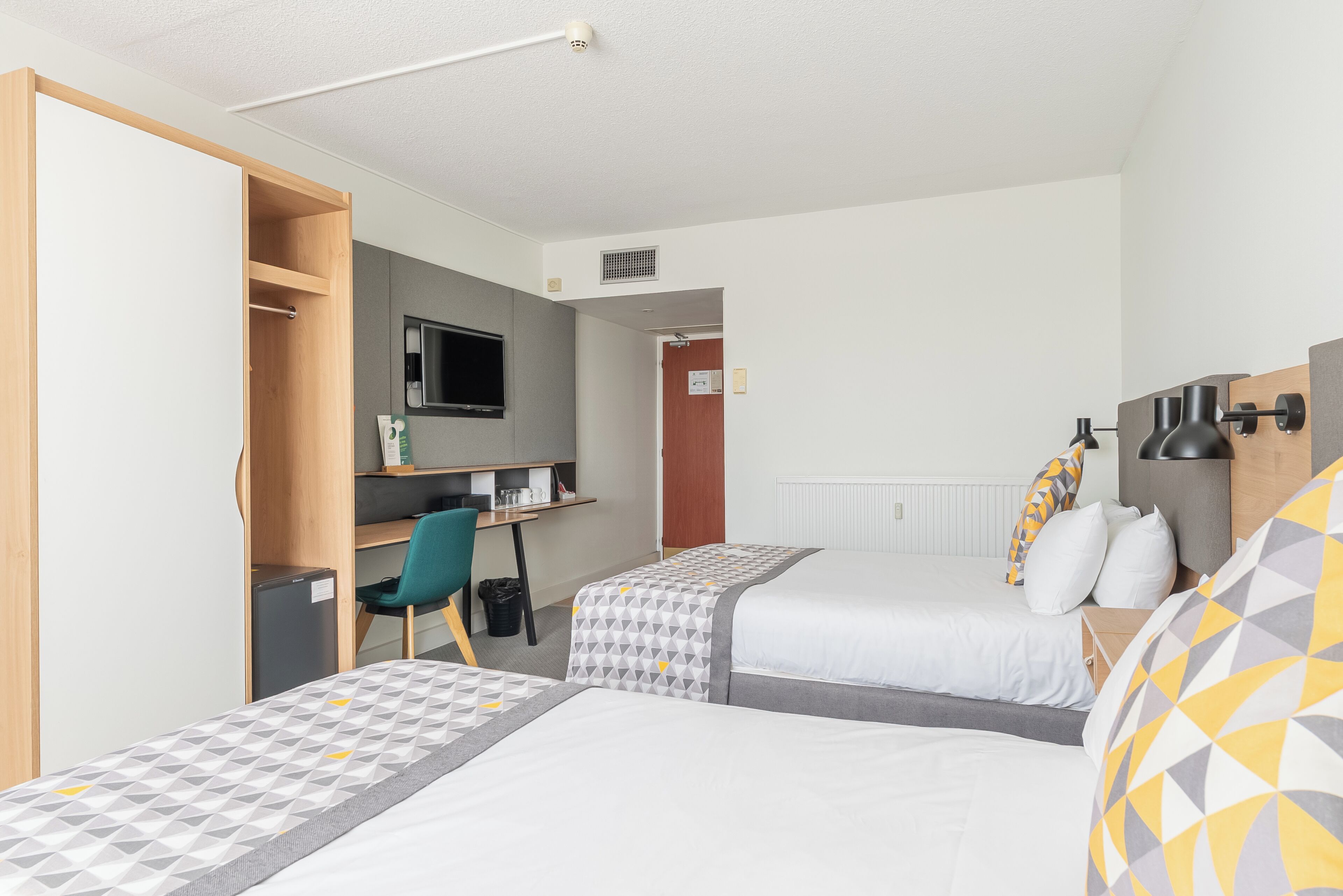 A hotel room with two beds, a desk, a chair, and a television.