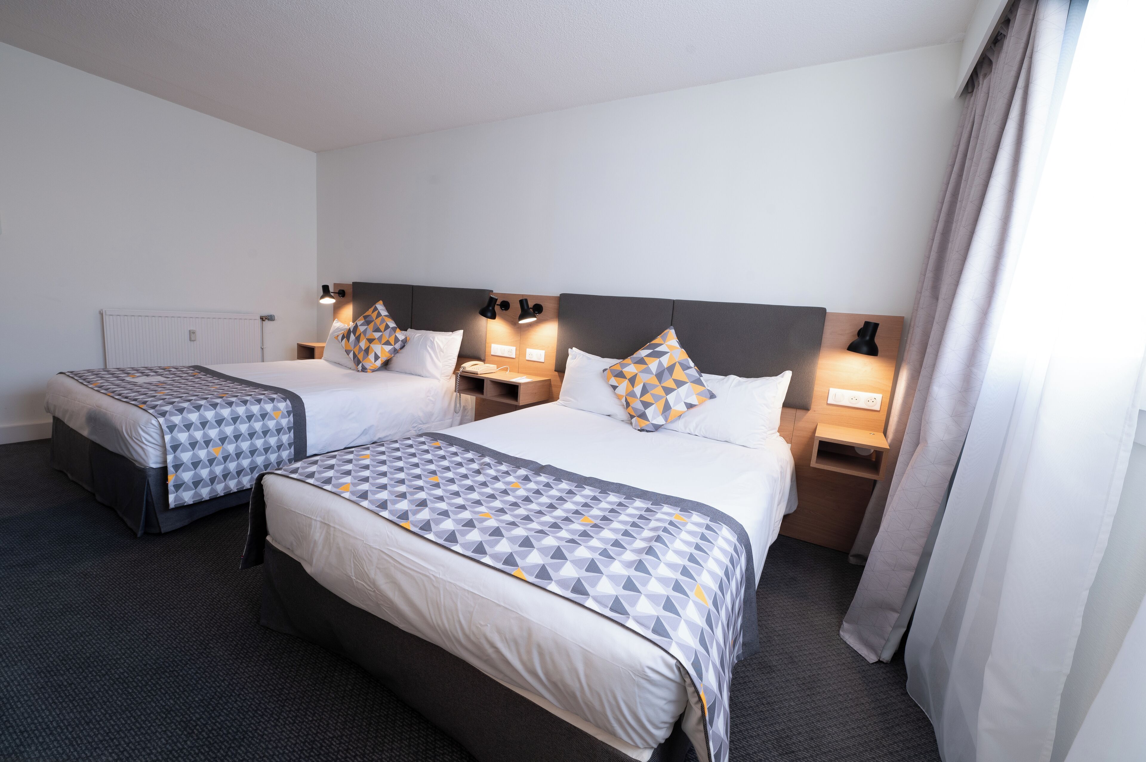 A hotel room with two beds, each with a patterned bedspread, bedside lamps, and a nightstand.