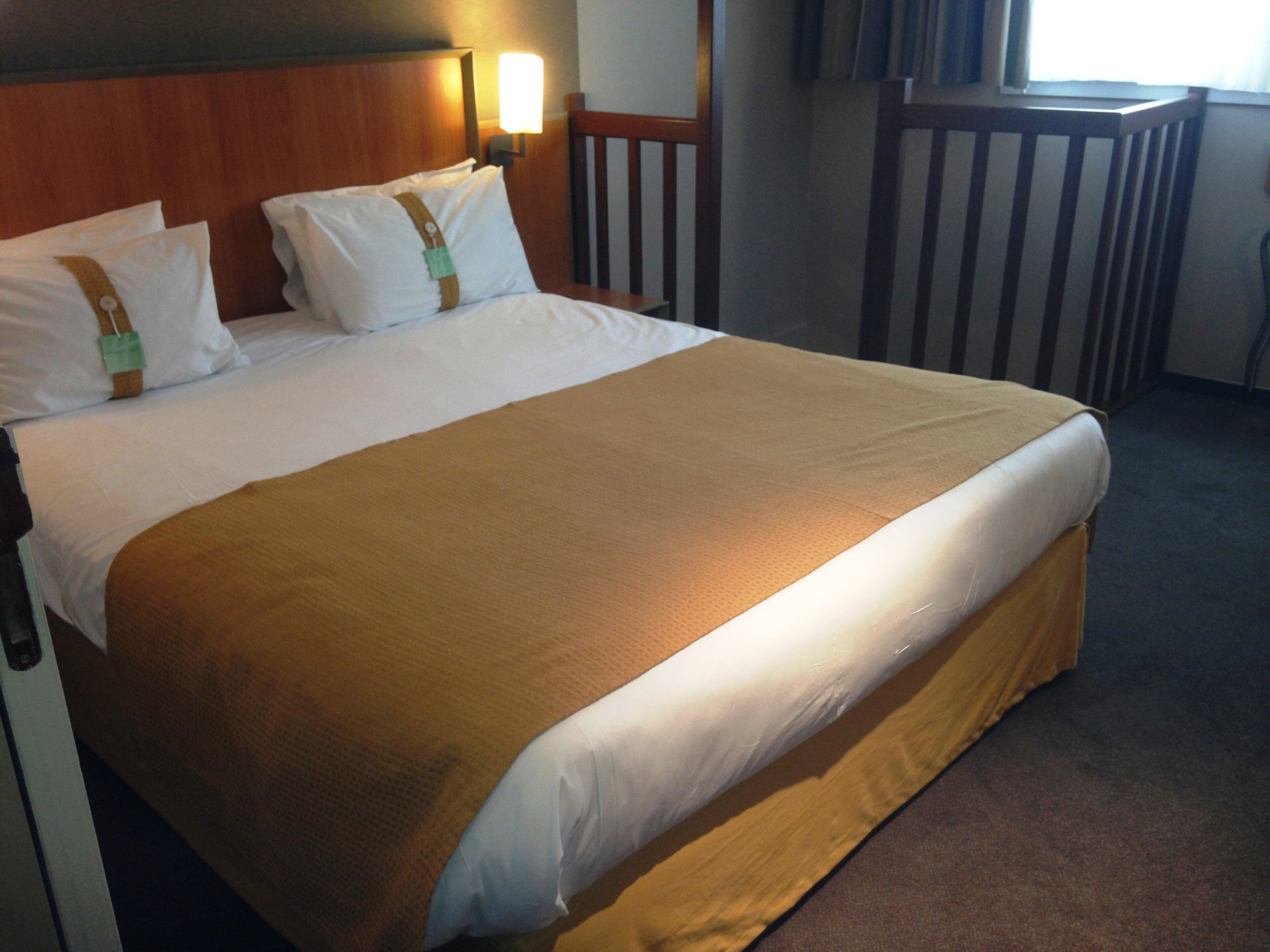 Una habitación de hotel con una cama grande, cabecera de madera y una mesita de noche con lámpara.