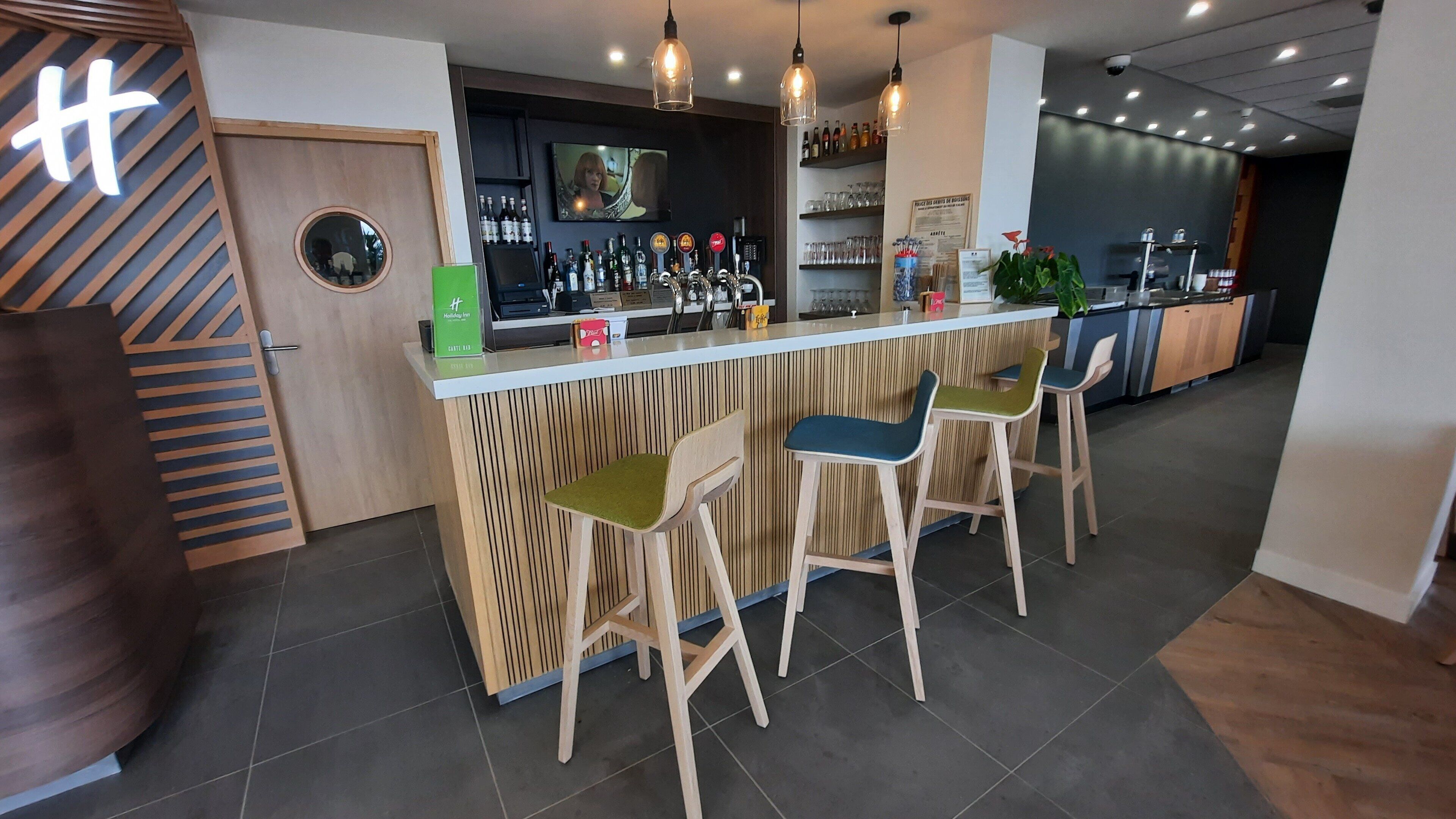 Eine Bar mit Holztresen, Barhocker und einer Auswahl an Flaschen.