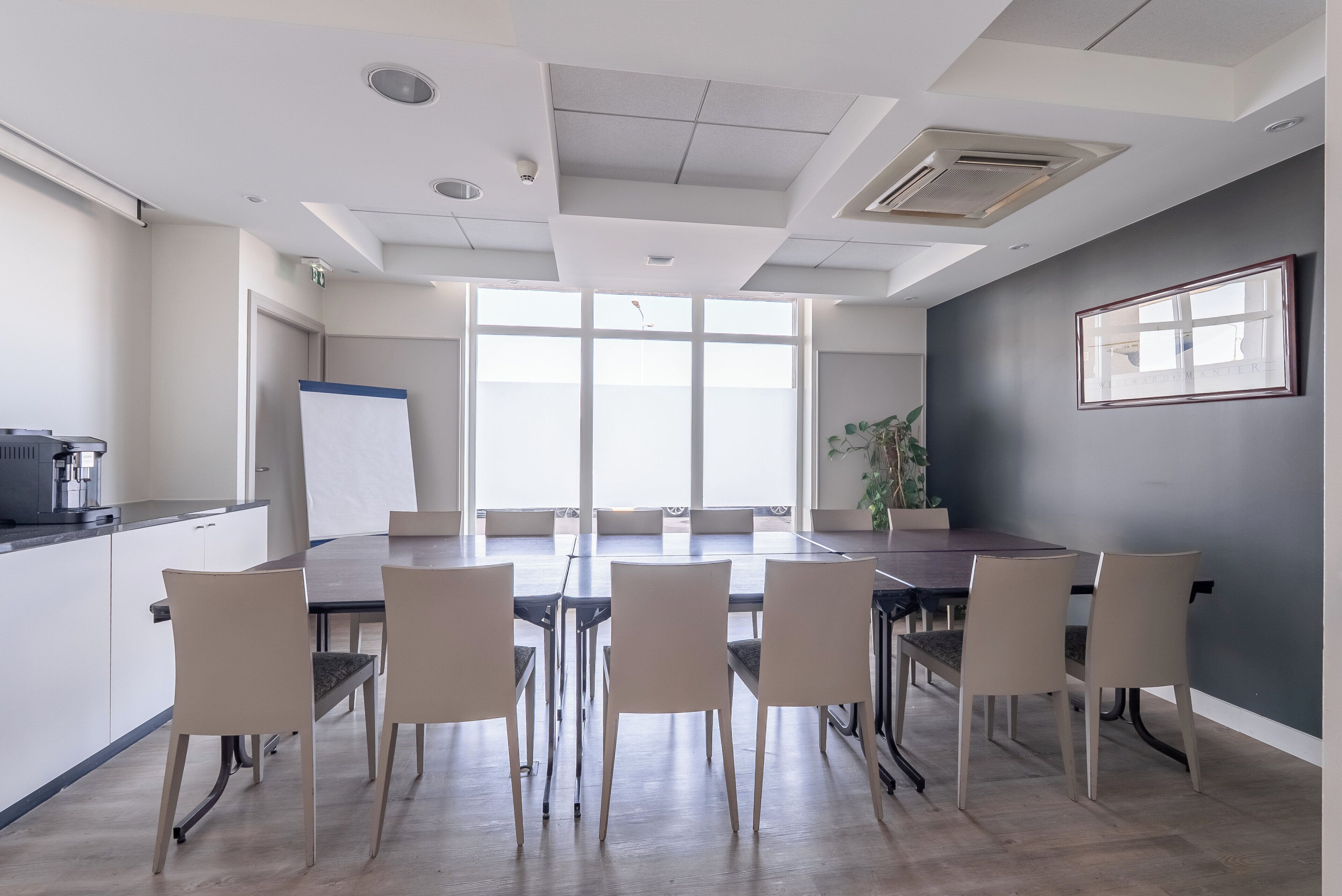 A conference room with a long table, six chairs, a whiteboard, and a large window.