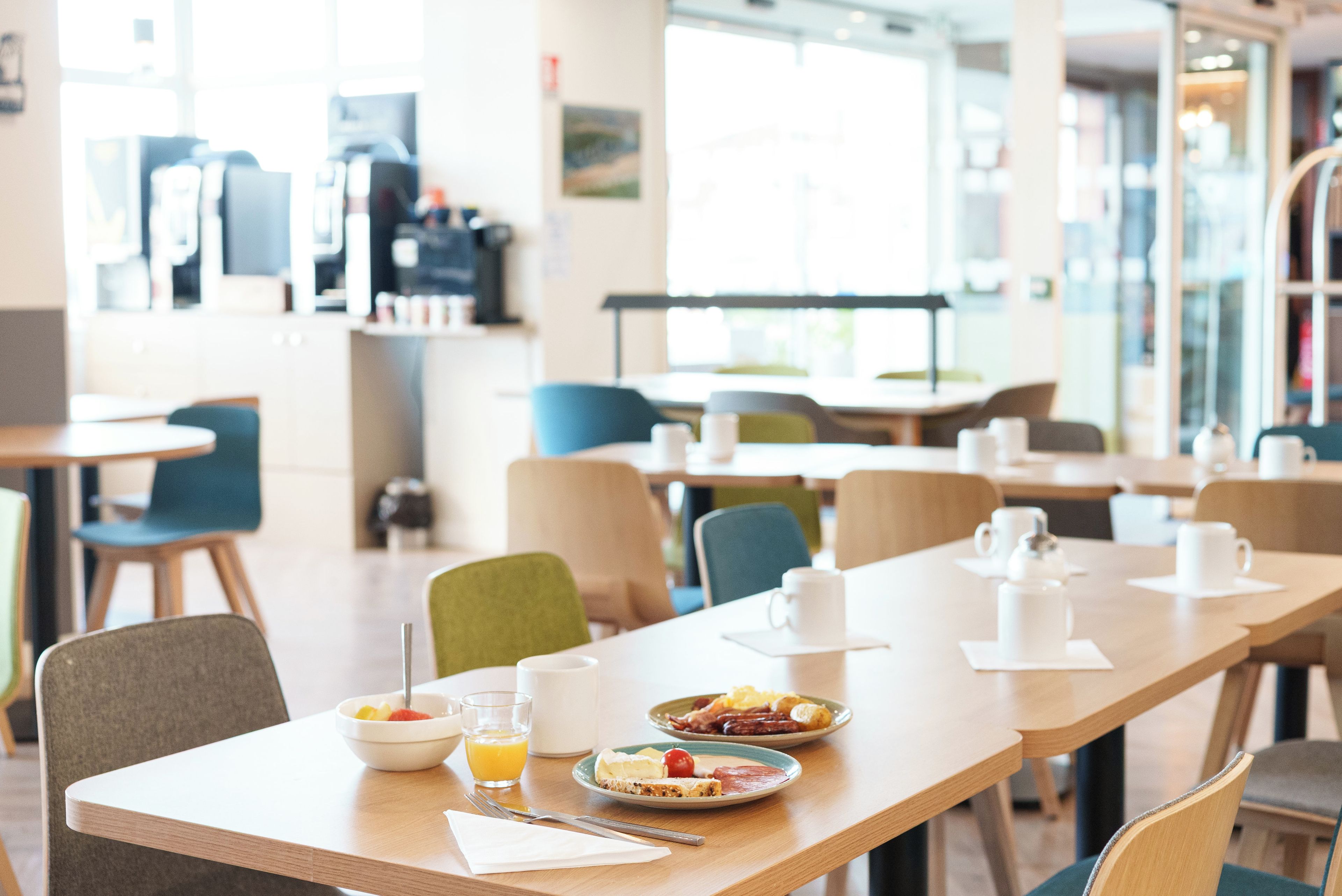 A dining area with tables and chairs, breakfast plates with eggs and toast, and a coffee machine in the background.