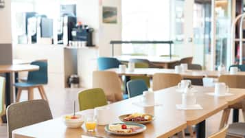 A dining area with tables and chairs, breakfast plates with eggs and toast, and a coffee machine in the background.