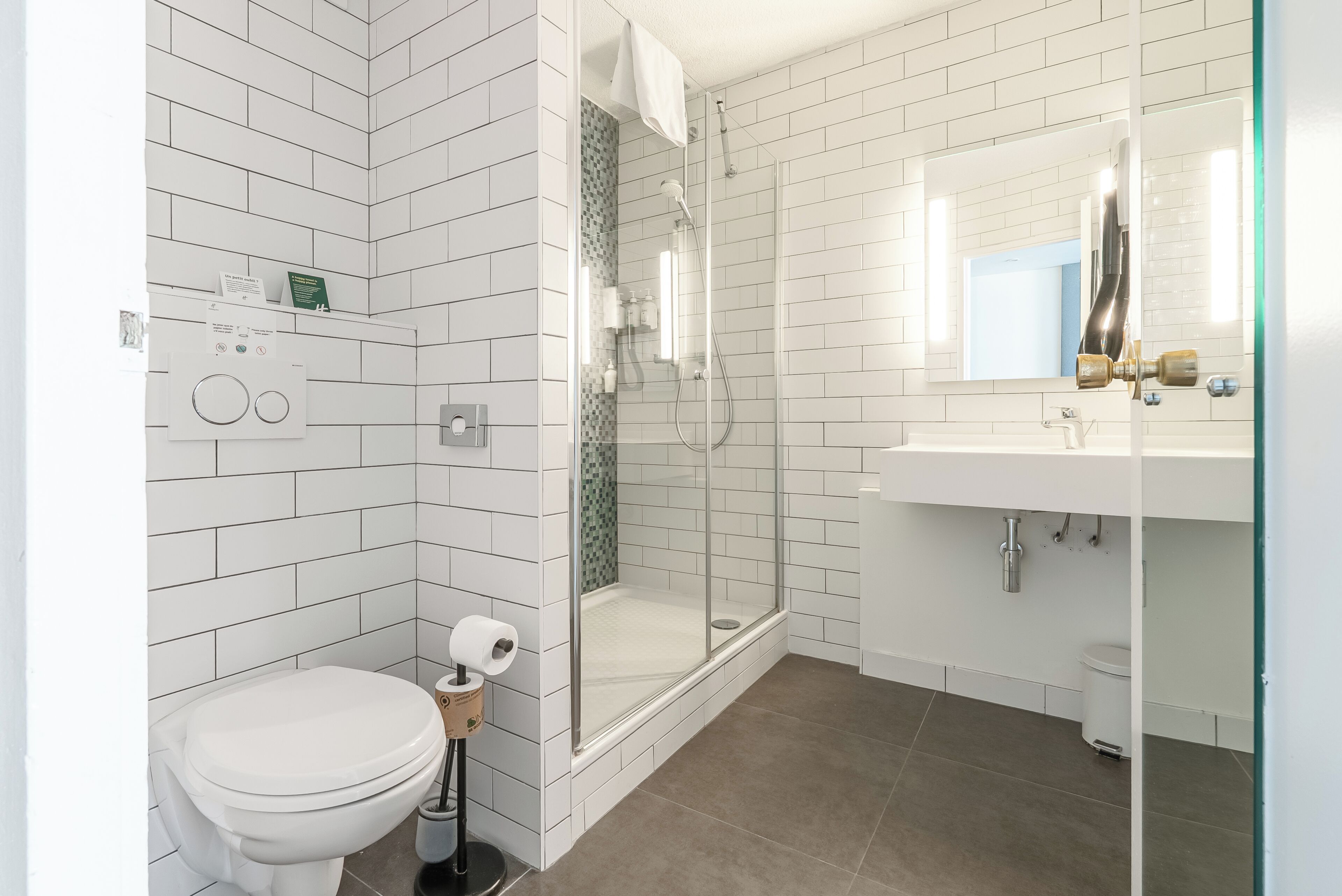 A modern bathroom with white tiles, a glass shower enclosure, a toilet, and a sink with a mirror.