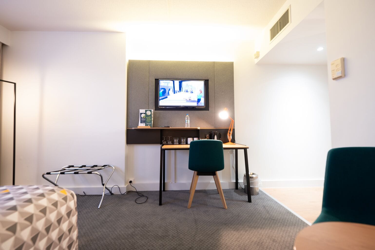 A modern hotel room with a desk, a television mounted on the wall, a chair, and a bed.