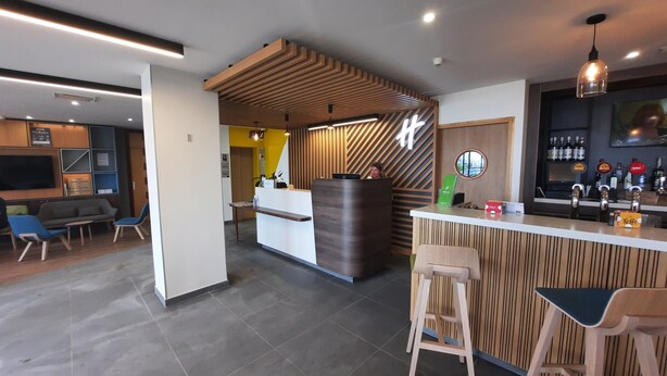 A modern bar area with a wooden reception desk, bar stools, and a seating area with a sofa and chairs.