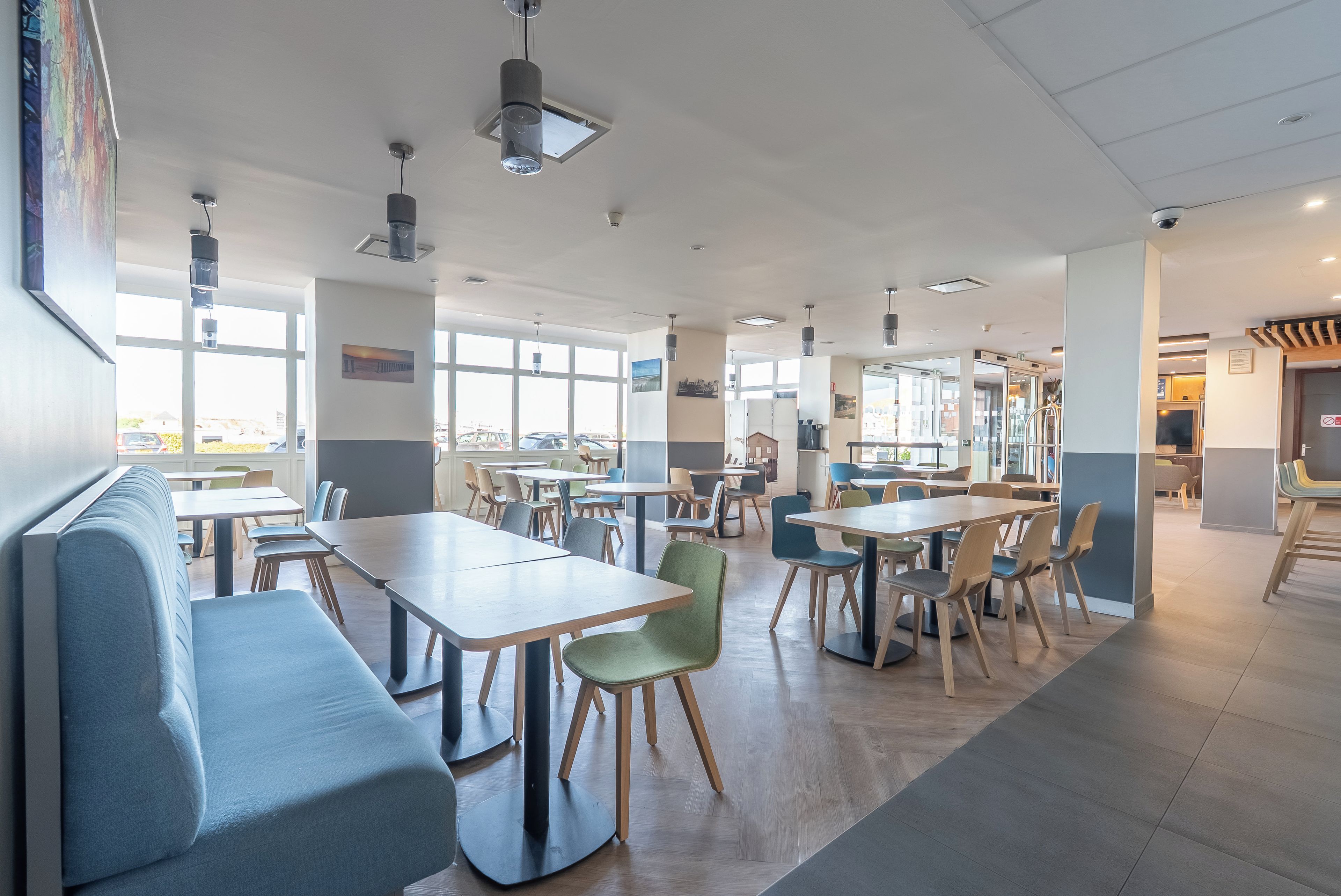 A spacious indoor area with multiple tables and chairs, large windows allowing natural light, and a variety of seating options including a long bench and individual chairs.