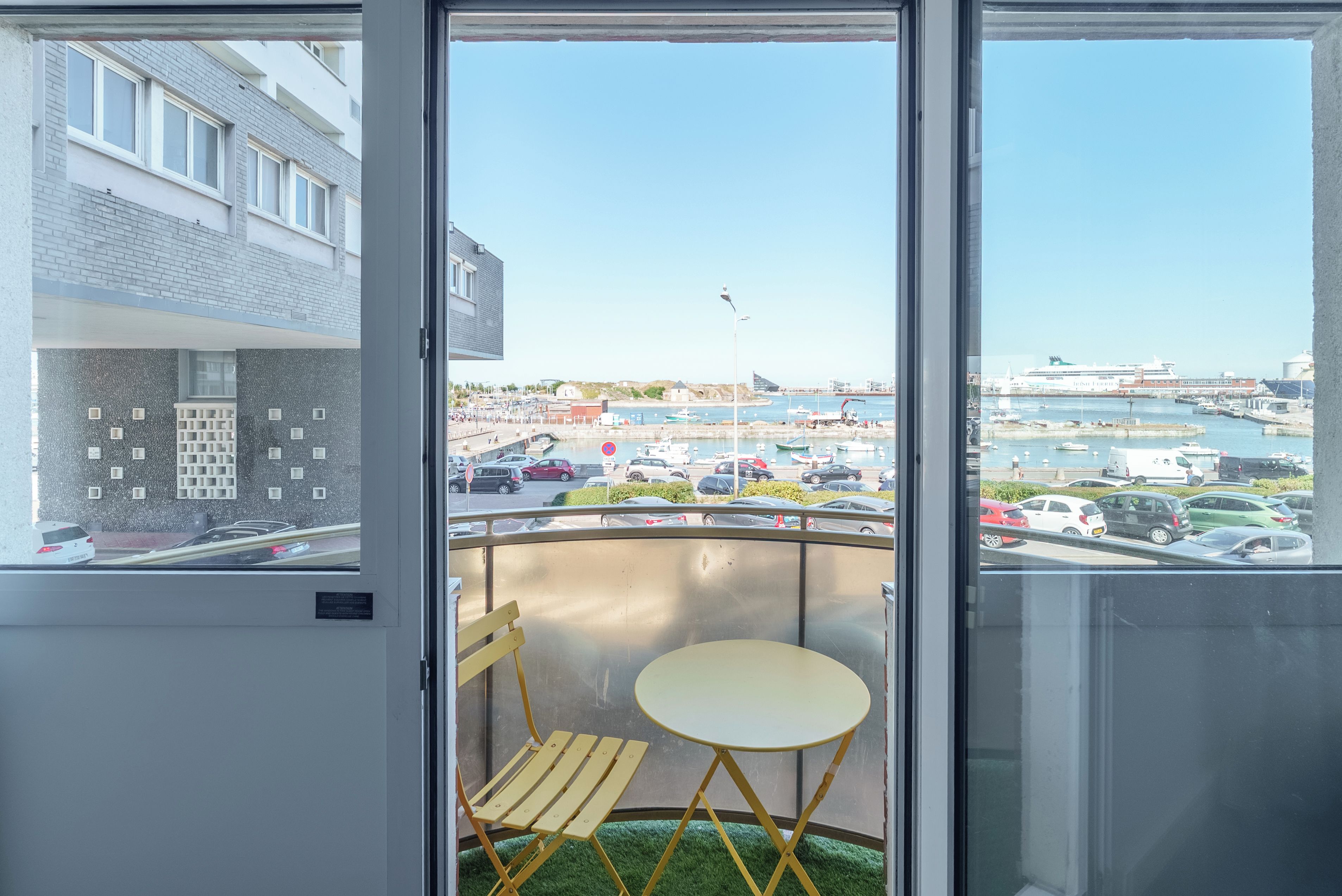 A balcony with a view of a marina, a table, and a chair.
