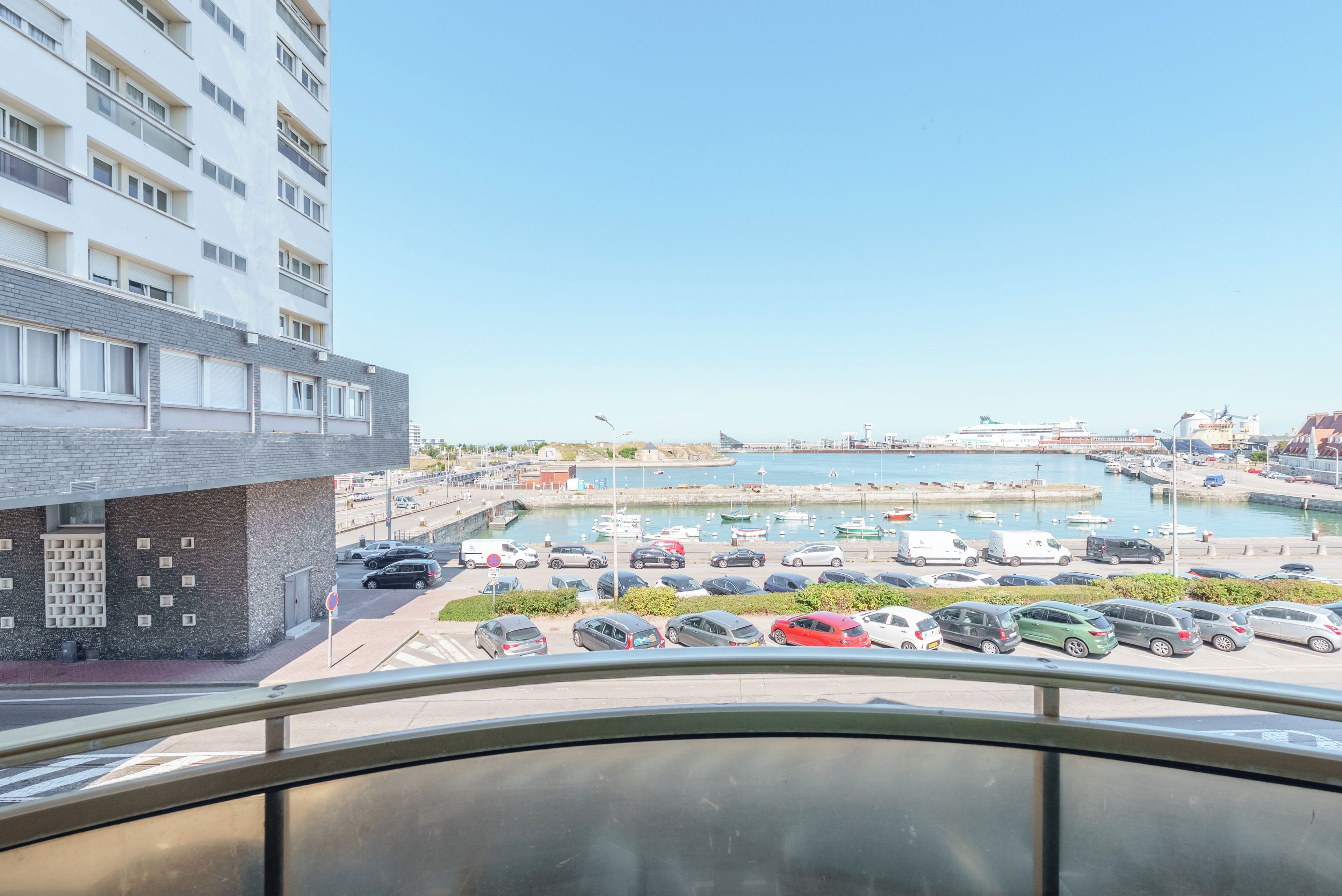 A view of a marina with boats, a parking area, and a building with a modern facade.