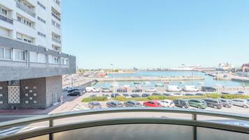 A view of a marina with boats, a parking area, and a building with a modern facade.
