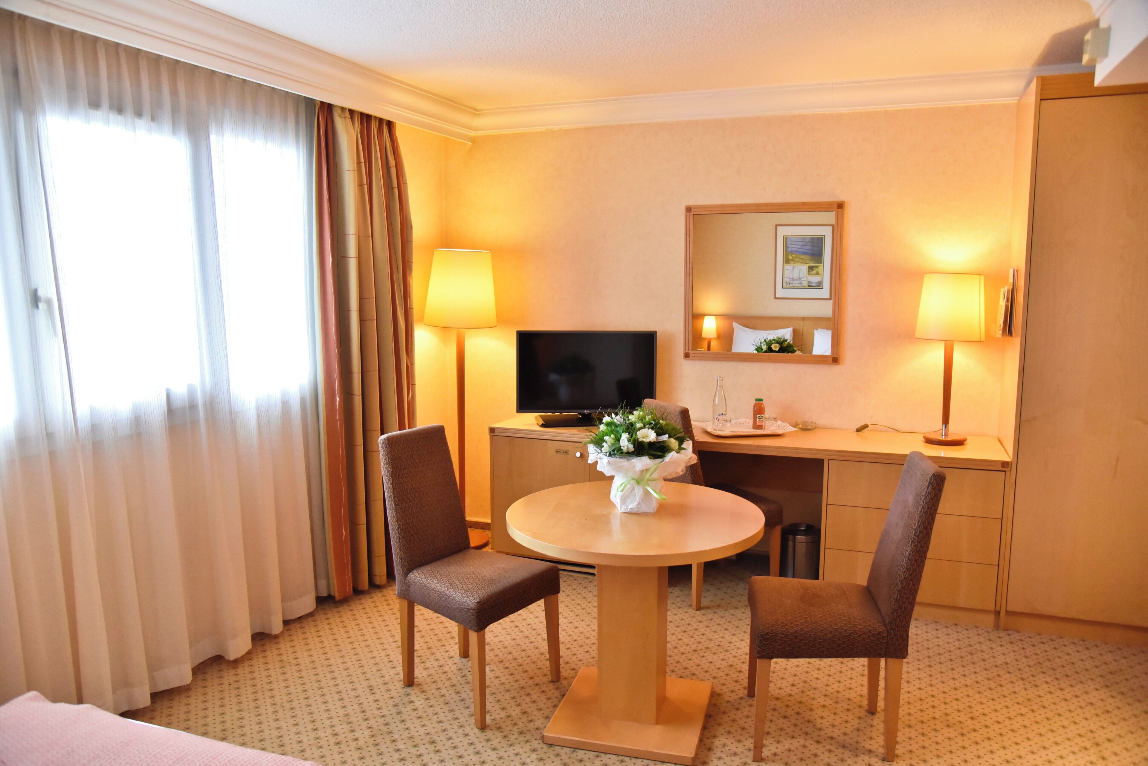 Une chambre d’hôtel avec une table ronde, deux chaises, un téléviseur, un bureau et un miroir.