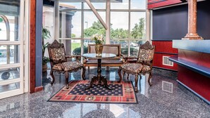 A lobby with a glass door, a round table with chairs, a red patterned rug, and a column. - Quality Inn & Suites Albany Airport (Latham)