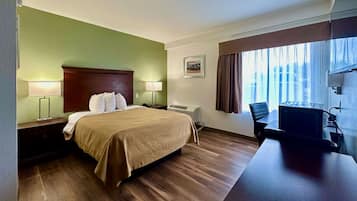 Habitación de hotel con cama, lámparas de noche, escritorio con silla, ventana con cortinas y televisor montado.