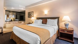 A hotel room with a large bed, a bathroom with a bathtub, and a mirror reflecting the room. - Quality Inn & Suites Albany Airport (Latham)