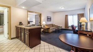 A hotel room with a kitchenette, a sofa, a dining table, and a large mirror. - Quality Inn & Suites Albany Airport (Latham)