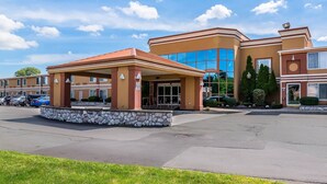 A hotel with a covered entrance, a stone wall, and a parking lot. - Quality Inn & Suites Albany Airport (Latham)