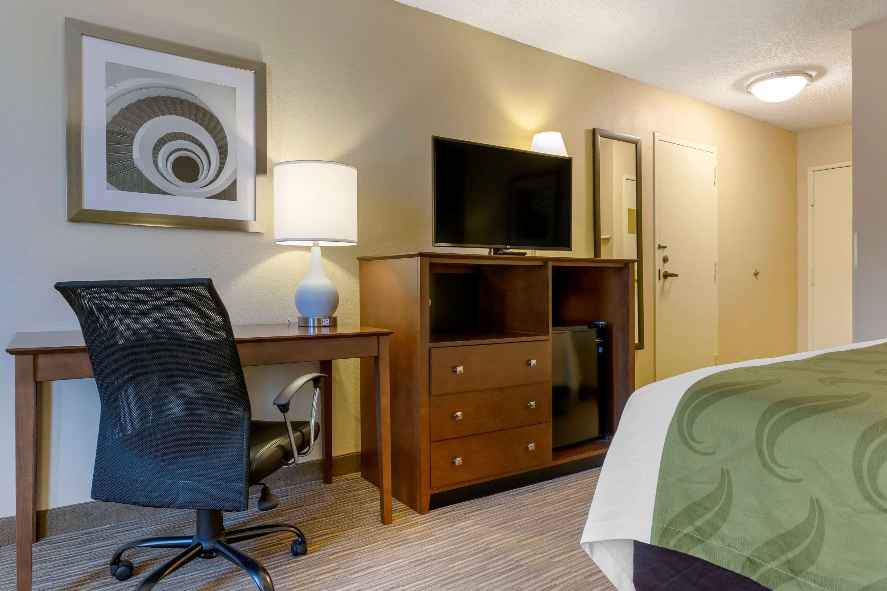 Une chambre d’hôtel équipée d’un lit, d’un bureau, d’une chaise, d’une télévision, d’une commode et d’un tableau encadré au mur.