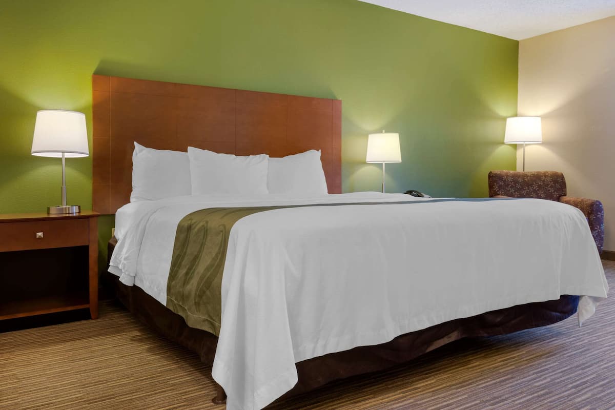 A hotel room with a large bed, two bedside tables with lamps, a chair, and a green wall.