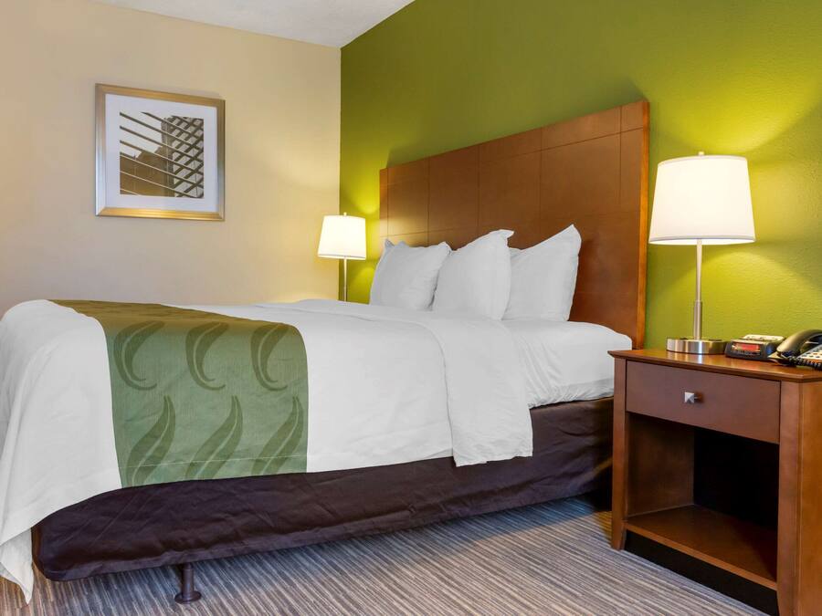 A hotel room with a bed, two bedside lamps, a nightstand with a phone, and a framed picture on the wall.