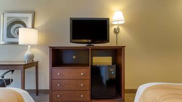 Habitación de hotel con cama, escritorio con lámpara, televisor sobre un soporte y minibar.