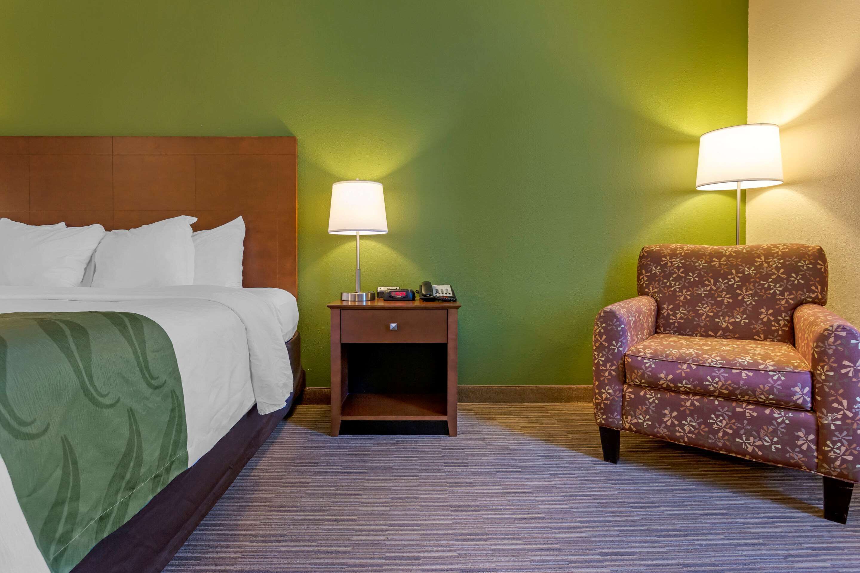 A hotel room with a bed, a nightstand with a lamp, and a floral armchair.