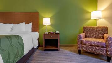 A hotel room with a bed, a nightstand with a lamp, and a floral armchair.